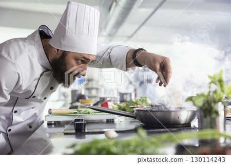 In a commercial kitchen, chef adding the finishing touches to a plated dish with fresh herbs. Expert uses raw vegetables, spices and essential kitchen equipment to create a tasty meal. 130114243