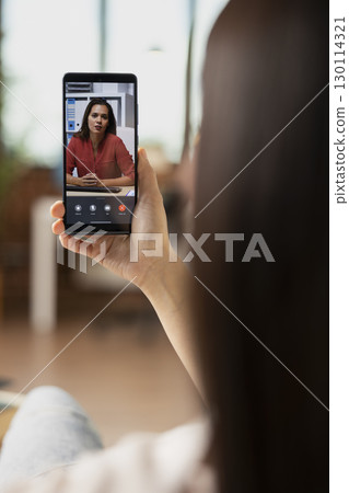 Self employed woman discussing with remote coworker on mobile device. Professional freelancer with smartphone in hand, brainstorming business project during virtual conversation with female investor. Self employed woman discussing with remote coworker on mobile device. Professional freelancer with smartphone in hand, brainstorming business project during virtual conversation with female investor. 130114321