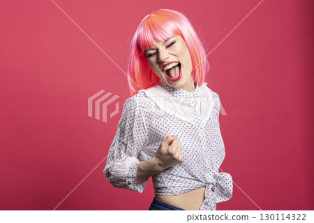 Joyful caucasian lady expressing excitement with mouth open and fist raised, standing isolated over pink background. Beautiful happy woman filled with enthusiasm, celebrating good news and success. 130114322