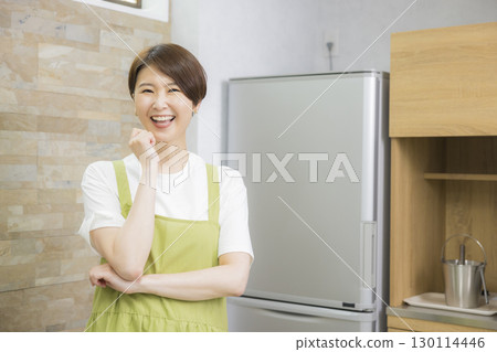 A woman in an apron opening a refrigerator 130114446