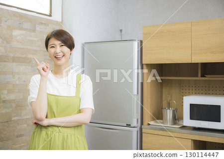 A woman in an apron opening a refrigerator A woman in an apron opening a refrigerator 130114447