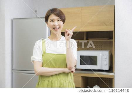 A woman in an apron opening a refrigerator A woman in an apron opening a refrigerator 130114448