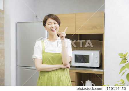 A woman in an apron opening a refrigerator A woman in an apron opening a refrigerator 130114450