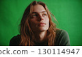 A person with long hair looking thoughtful with a green backdrop enhancing the friendly vibe 130114947