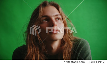 A person with long hair looking thoughtful with a green backdrop enhancing the friendly vibe 130114947
