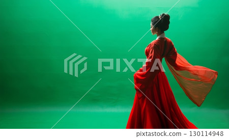 A figure in elegant traditional garments exuding grace in front of a rich green backdrop 130114948