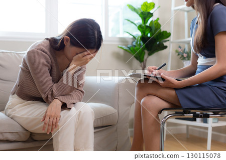 Emotional crisis concept. young Asian woman covers her face in distress during therapy session, while female therapist takes notes, expressing pain, depression and mental health struggle. Emotional crisis concept. young Asian woman covers her face in distress during therapy session, while female therapist takes notes, expressing pain, depression and mental health struggle. 130115078