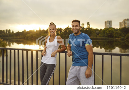 Couple in sportswear standing on a bridge at sunset and smiling, close-up Couple in sportswear standing on a bridge at sunset and smiling, close-up 130116042