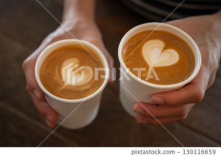 Cropped shot view of someone holding couple cups of cappuccino coffee before drinking. A cappuccino is the perfect balance of espresso, steamed milk and foam. 130116659