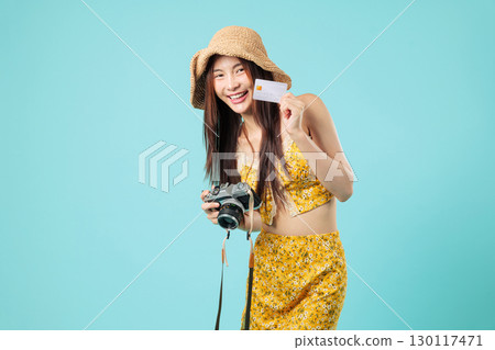Happy Asian woman ready to travel, holds her bank credit card, camera and blank payment card to make online payment, cheerful tourism holiday smile girl, headshots isolated studio blue background 130117471
