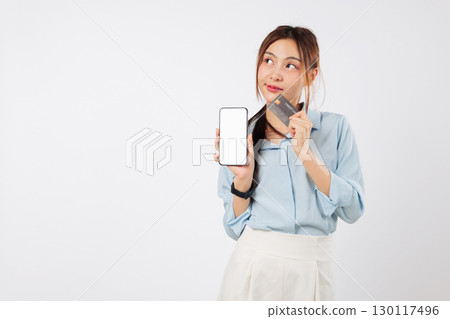 Asian woman thoughtfully holds a phone, credit shop bank card for online payment finance, later she may thinking about another card and its uses. isolated studio white background Asian woman thoughtfully holds a phone, credit shop bank card for online payment finance, later she may thinking about another card and its uses. isolated studio white background 130117496