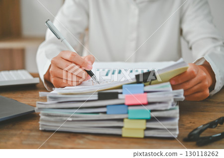 A person is writing on a stack of papers with a pen 130118262