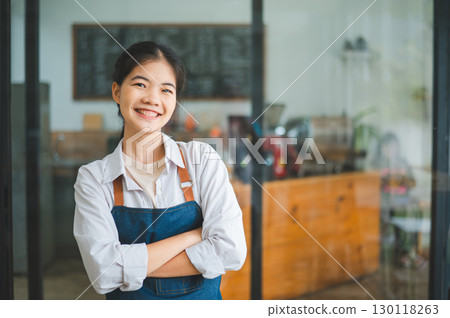 Smiling Asian coffee shop owner standing in front of cashier counter.welcome customers who come in to place orders in the cafe. Smiling Asian coffee shop owner standing in front of cashier counter.welcome customers who come in to place orders in the cafe. 130118263