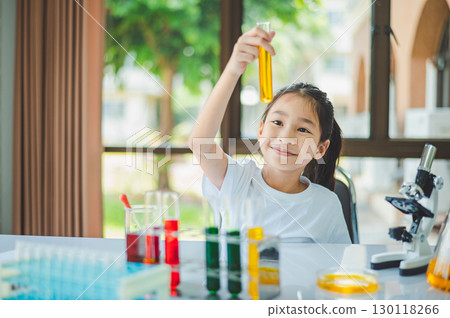 little scientist looking through a microscope and test tubes filled with chemicals for learning about science and experiments. little scientist looking through a microscope and test tubes filled with chemicals for learning about science and experiments. 130118266