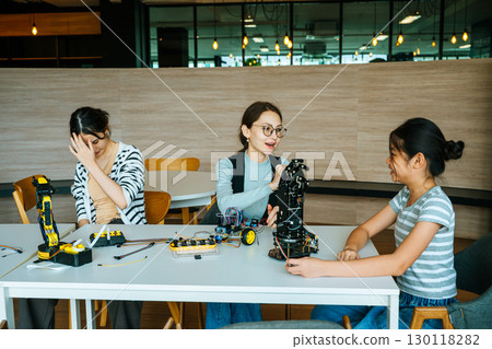 Mentor guiding girls building robotic arm together in modern STEM learning environment 130118282