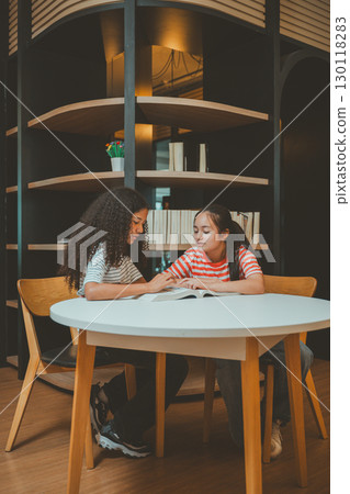 Teenage girls studying together in modern library showing concentration teamwork and educational motivation Teenage girls studying together in modern library showing concentration teamwork and educational motivation 130118283