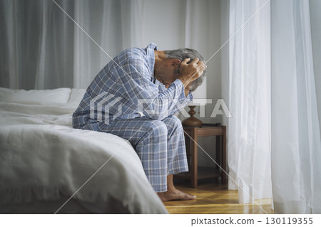 Senior man in pajamas sitting on bed and holding his head 130119355