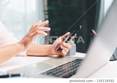 Close-up shot, woman sits at a wooden table using her smartphone, with her finger touching the phone screen as she navigates mobile banking, online shopping, and social media networks. Close-up shot, woman sits at a wooden table using her smartphone, with her finger touching the phone screen as she navigates mobile banking, online shopping, and social media networks. 130119582