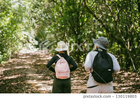 Two female friends with backpacks on vacation hiking through countryside together. Asian friend girls backpacker friend travel in forest wild together. happy and enjoying sunny day while hiking. 130119803