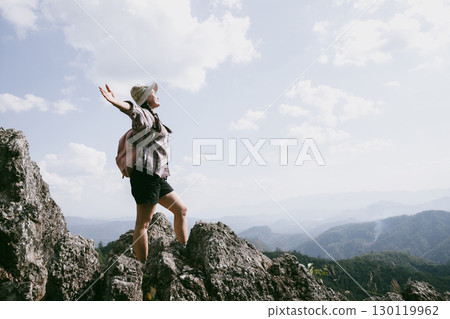 Woman hiker on top of mountain. Hiker with arms up on top of mountain successful young woman enjoying triumph. traveler exploring world. Hikers with backpacks relaxing. Sport and success concept. 130119962