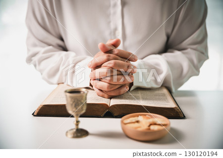 During the holy communion ceremony in church, a hand is extended in faith to receive the sacred sacrament, reflecting the spiritual and religious worship central to Christianity. 130120194