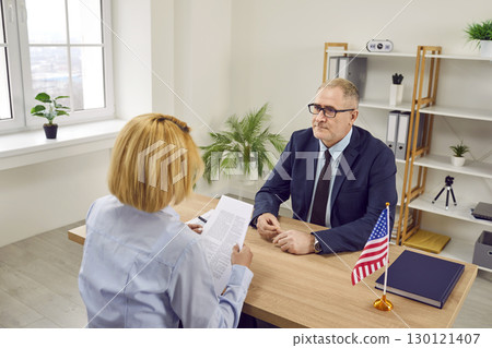 Woman sitting back in office of US public services or embassy and having visa interview. 130121407