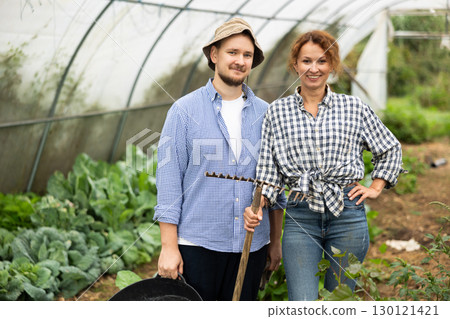 Man and woman with rakes in hands inside greenhouse with vegetable harvest Man and woman with rakes in hands inside greenhouse with vegetable harvest 130121421