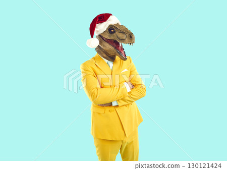 Man in yellow suit, funny dinosaur mask and Christmas hat standing on blue background 130121424