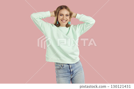 Happy, smiling young woman, dressed in light mint sweater and blue jeans, dances and throws her hands behind her head. Happy, smiling young woman, dressed in light mint sweater and blue jeans, dances and throws her hands behind her head. 130121431