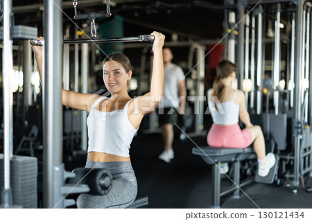 Slender athletic woman work out muscles of hands on cable crossover machine in fitness club 130121434