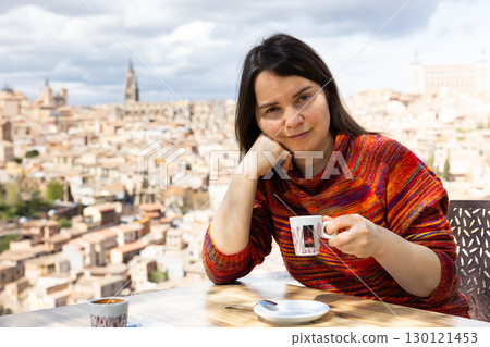 Portrait of a woman traveler sitting at a table and holding a cup of coffee Portrait of a woman traveler sitting at a table and holding a cup of coffee 130121453