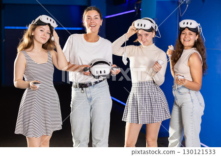 Four smiling girlfriends with virtual reality devices stand and pose in gaming modern club Four smiling girlfriends with virtual reality devices stand and pose in gaming modern club 130121533