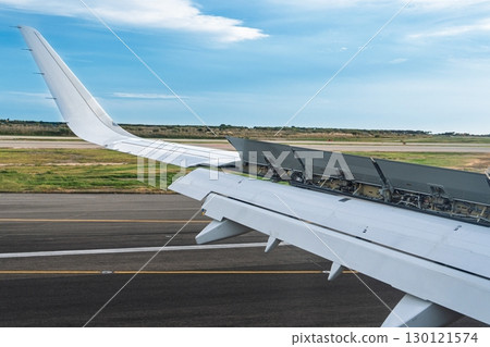Airplane Wing with Flaps Extended on Runway at Airport During Landing, Blue Sky Above 130121574
