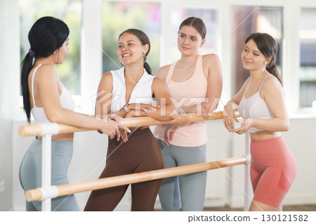 Group of young girls relax and talking after ballet exercises near ballet barre in gym. Health and fitness concept 130121582