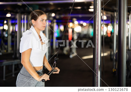 Slender athletic woman work out muscles of hands on cable crossover machine in fitness club Slender athletic woman work out muscles of hands on cable crossover machine in fitness club 130121678