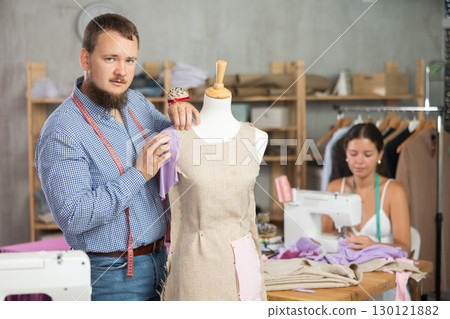 Tailor shaping dress on mannequin in fashion studio with colleague 130121882