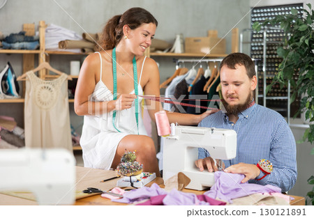 Flirty female colleague teasing shy male tailor Flirty female colleague teasing shy male tailor 130121891