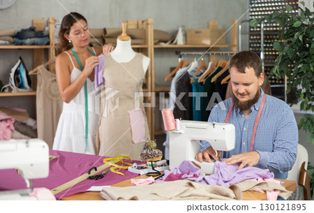 Tailor sewing at machine while colleague working with mannequin 130121895