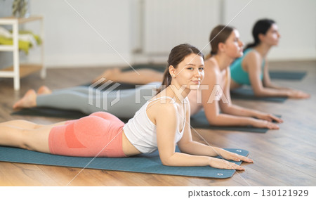 Women bending in back while lying on stomach in Bhujangasana Cobra Stretch position during training together in studio Women bending in back while lying on stomach in Bhujangasana Cobra Stretch position during training together in studio 130121929