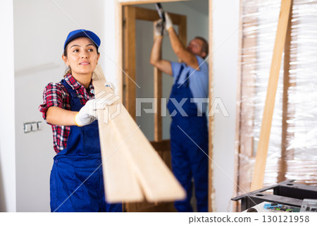 Positive woman builder carrying wooden planks in construction site 130121958