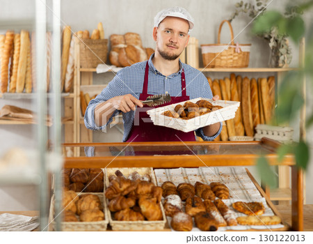 Selling fresh croissants in bakery - Baker places hot croissants on display Selling fresh croissants in bakery - Baker places hot croissants on display 130122013