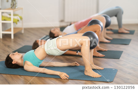 Young girl practicing Pilates bridge with exercise ball at group session Young girl practicing Pilates bridge with exercise ball at group session 130122056