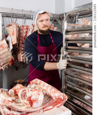 Portrait of male butcher while working in a butcher shop - moving trays with chopped carcasses 130122085