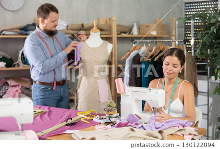 Male dressmaker working with mannequin while girl sews 130122094
