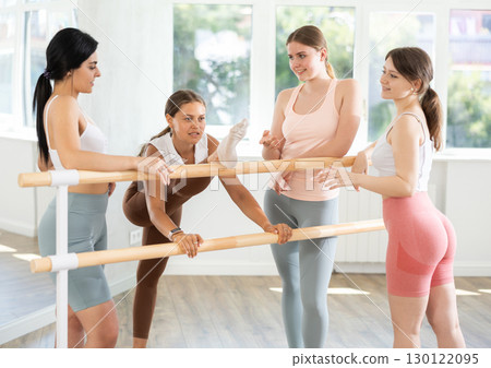 Young ballerinas chatting joyfully standing around training barre 130122095