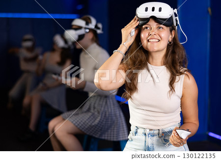 Excited young woman with VR glasses and controllers in gaming room 130122135