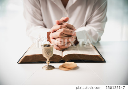 During the holy communion ceremony in church, a hand is extended in faith to receive the sacred sacrament, reflecting the spiritual and religious worship central to Christianity. 130122147