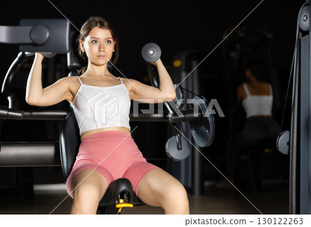 Athletic woman work out muscles of arms and hands on simulator in fitness club 130122263