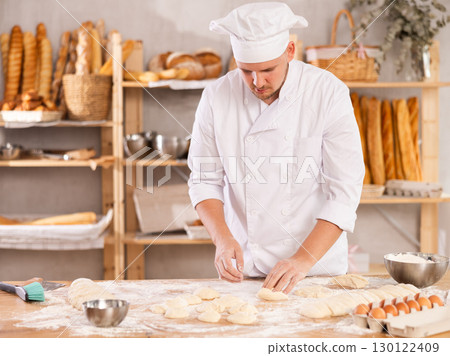 Professional baker stands at his work bench, kneading and shaping dough to make bread and baguettes Professional baker stands at his work bench, kneading and shaping dough to make bread and baguettes 130122409