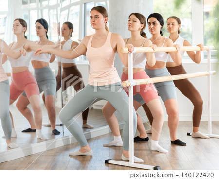 Active dancing young girls engaged in group classes perform demi plie pose near ballet barre in gym 130122420